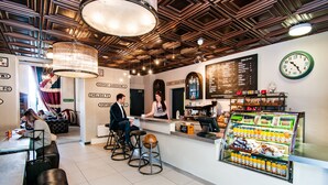 A modern cafe with a barista station, seating area, and a display case with beverages. - Rest Up London - Hostel (London)