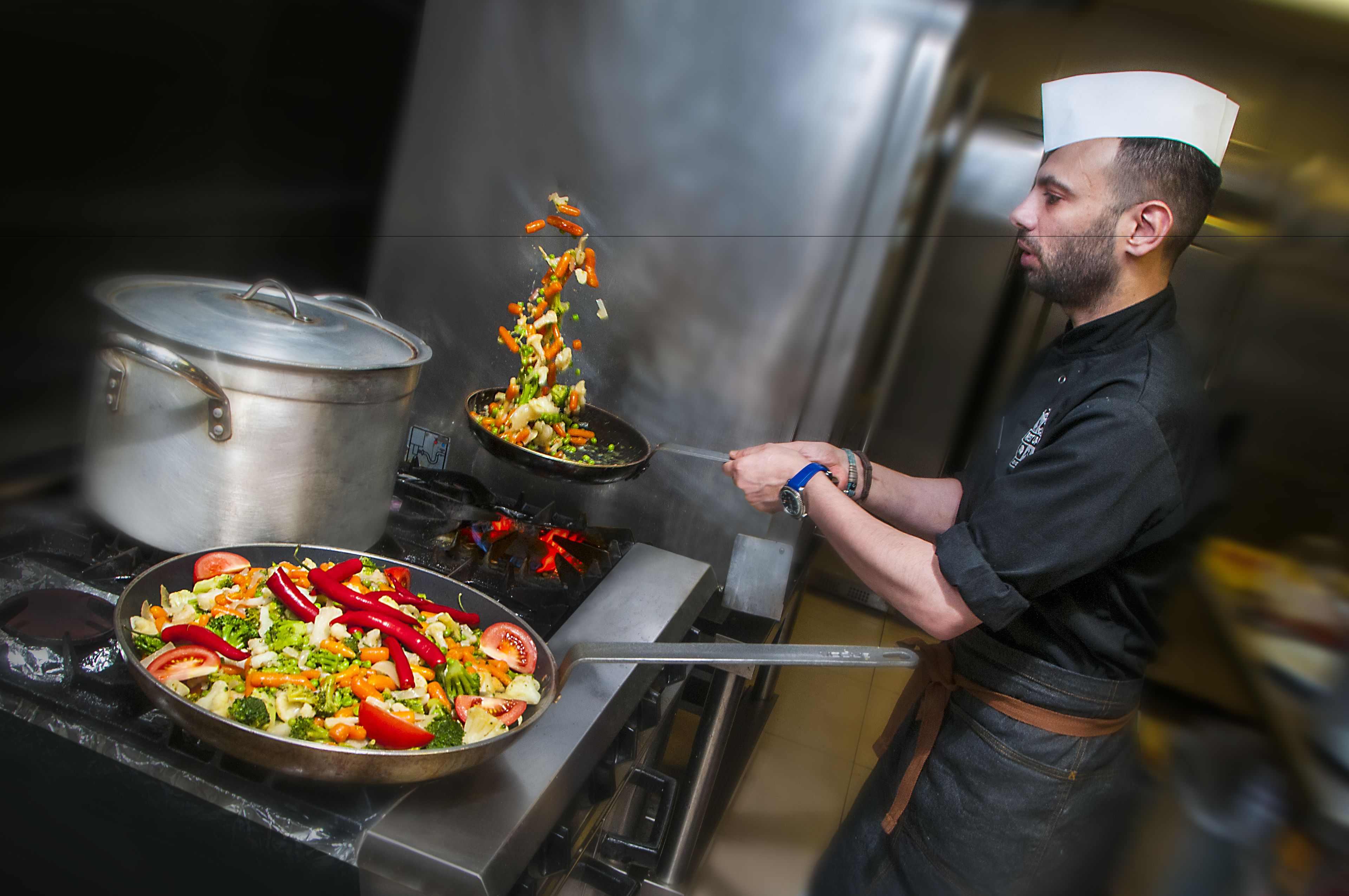 A chef cooking with vegetables and a pot on a stove.