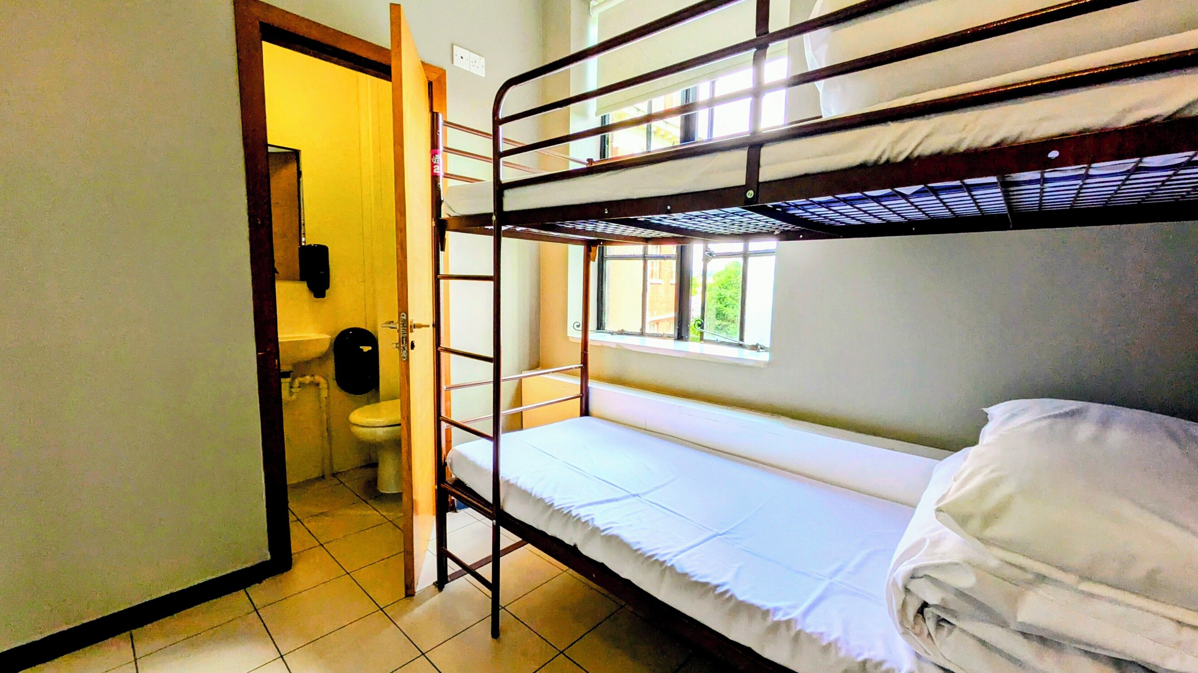 A dormitory room with bunk beds, a toilet, and a window.