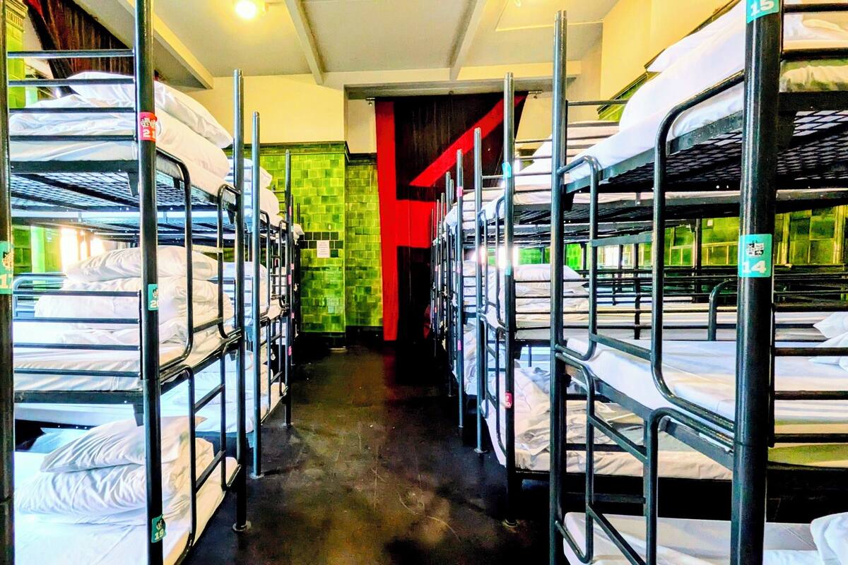 A corridor with bunk beds lined on both sides, a green tiled wall, and a red door at the end.