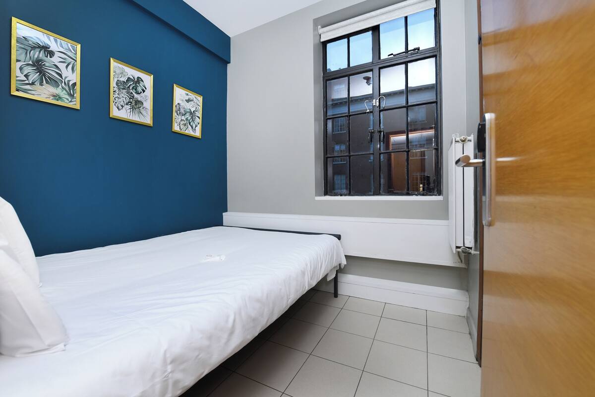 A bedroom with a bed, a window, and three framed botanical prints on the wall.