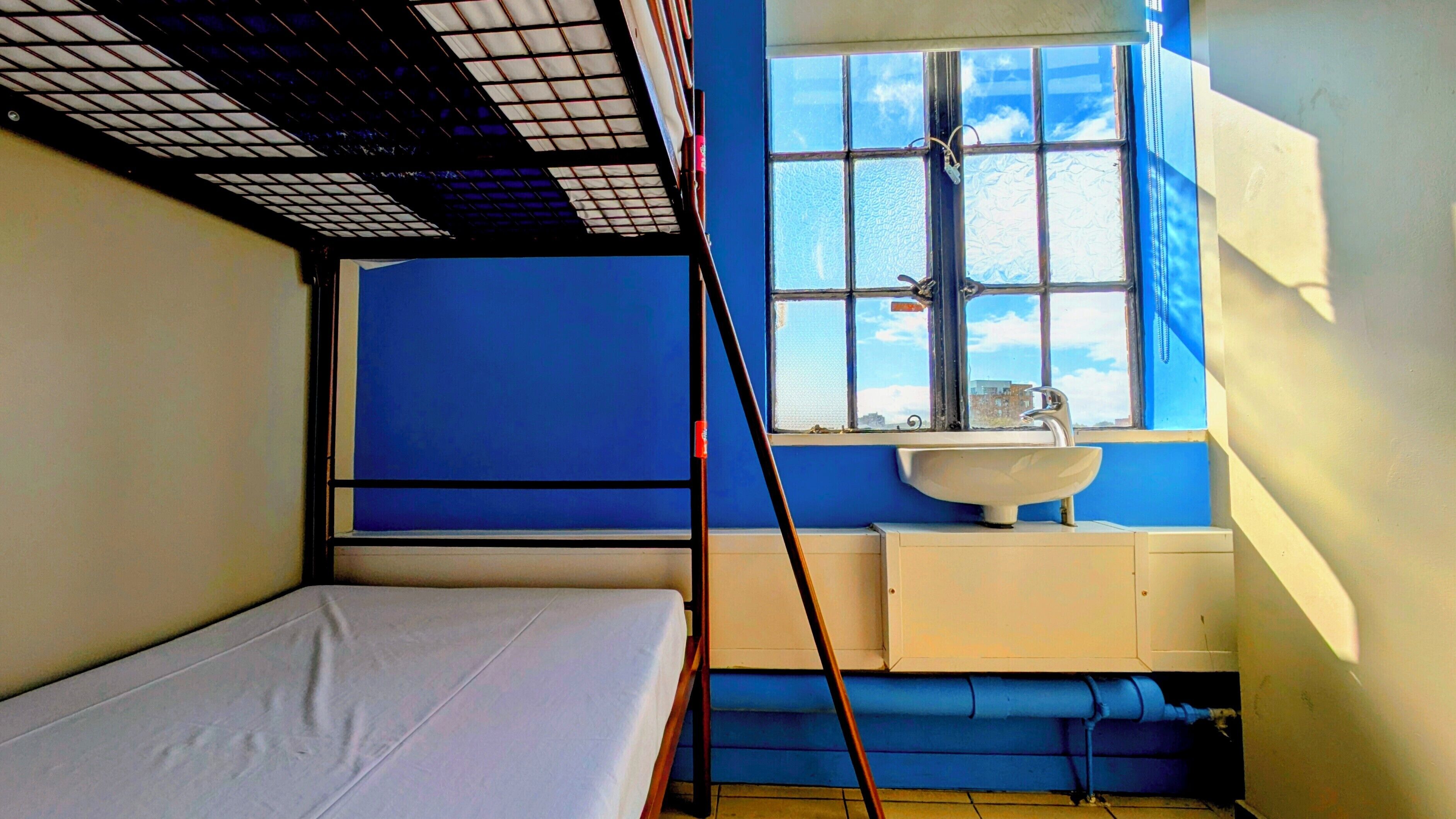 A small, compact room with a bunk bed, a window with frosted glass, a sink, and a blue wall.