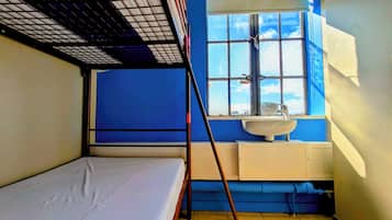 A small, compact room with a bunk bed, a window with frosted glass, a sink, and a blue wall.