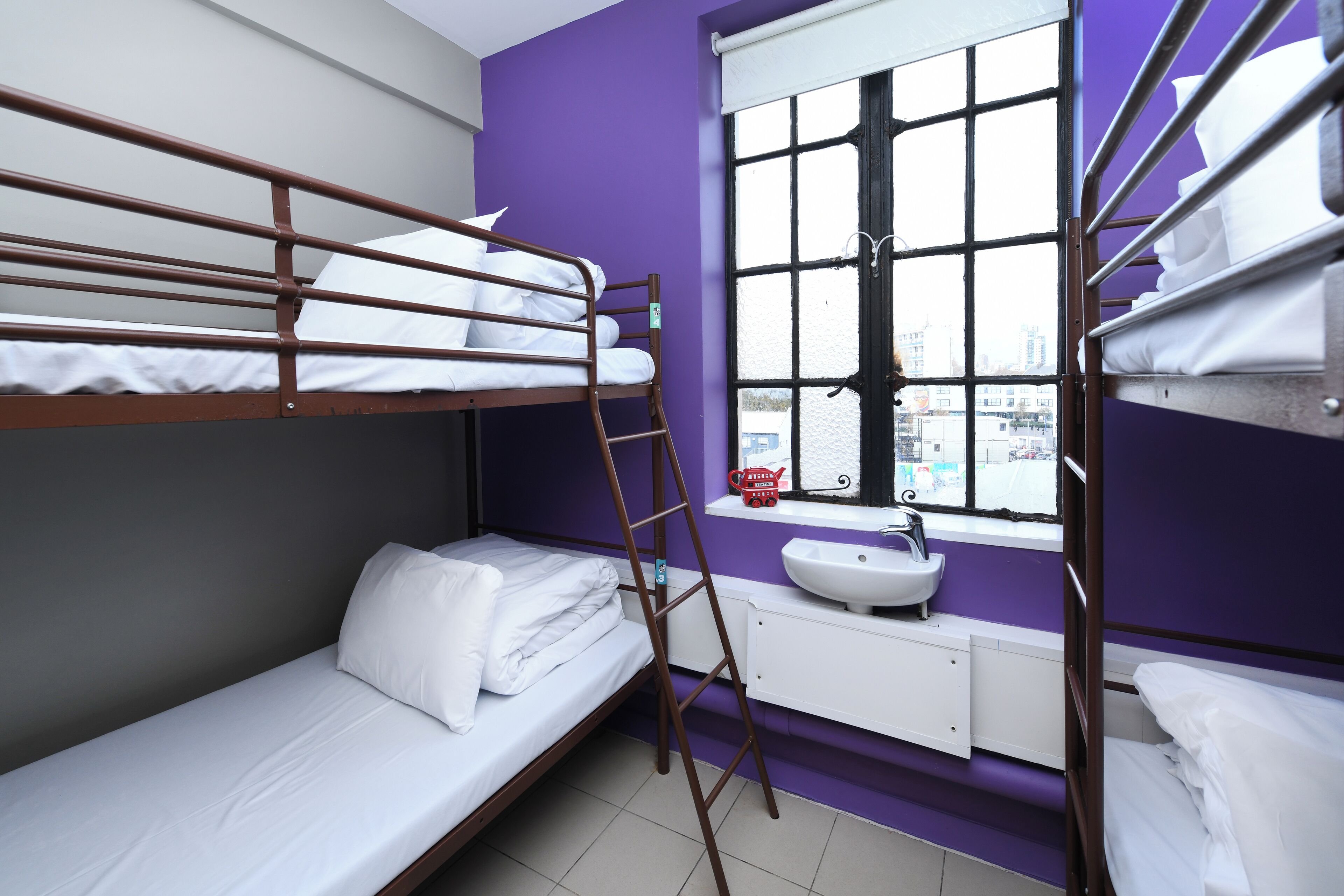 Une chambre avec un lit superposé, une fenêtre, un lavabo et une vue sur la ville.