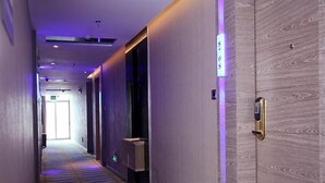 A hotel hallway with a patterned carpet, a door with a keypad lock, and a lighted wall panel. - GreenTree Alliance Shenzhen Shekou Sea World Hotel (Shenzhen)