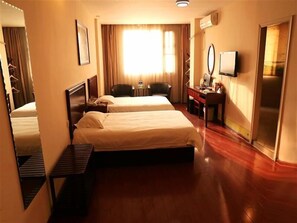 Une chambre d’hôtel avec deux lits, un bureau avec une chaise, une petite table, un miroir et une armoire.