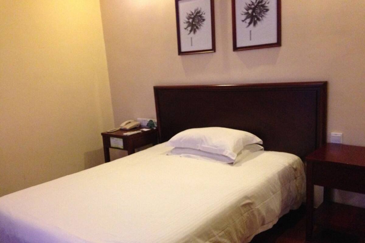 Ein Hotelzimmer mit einem Einzelbett, einem Nachttisch mit Telefon und zwei gerahmten Bildern an der Wand.