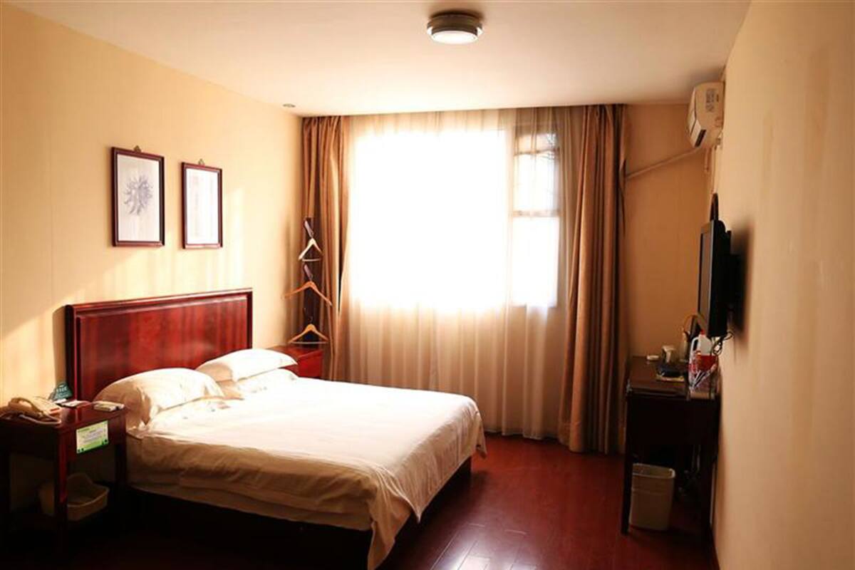 Ein Hotelzimmer mit Bett, Schreibtisch, Stuhl, Fernseher und einem fenster mit Vorhängen.