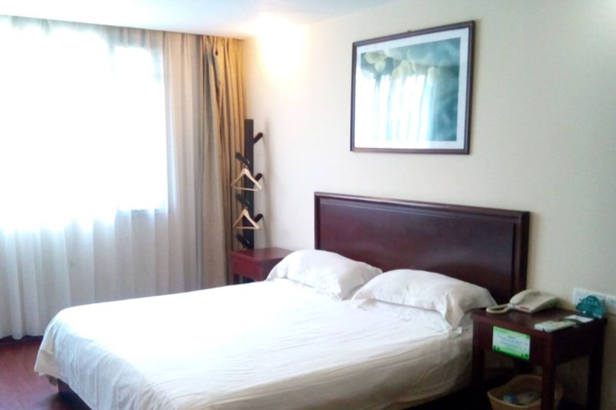 Ein Hotelzimmer mit einem Bett, einem Nachttisch, einem Telefon und einem Gemälde an der Wand.