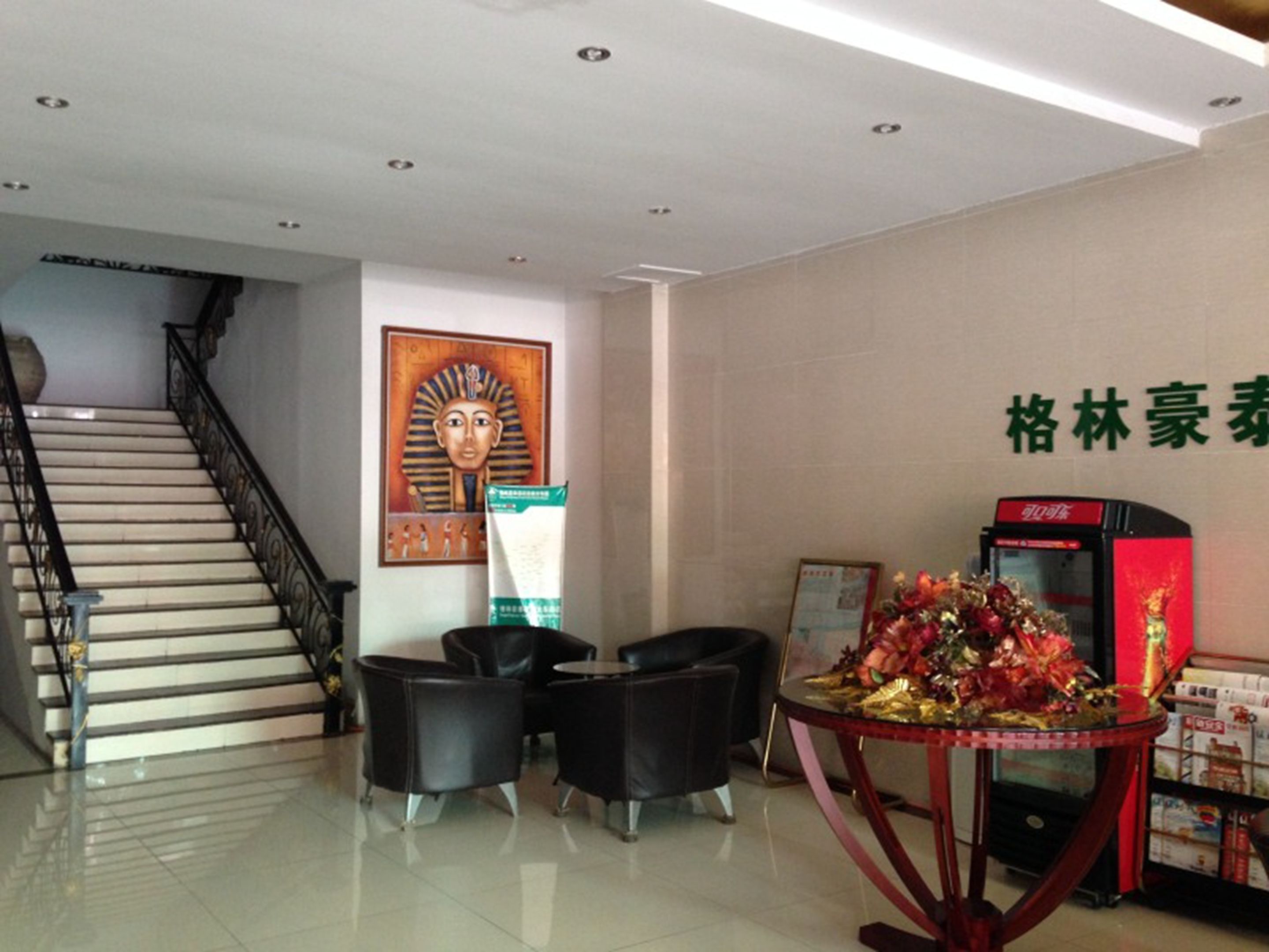 Eine Lobby mit einer Treppe, einem Poster, einem Tisch mit einer Blumenkomposition und einem Automaten.