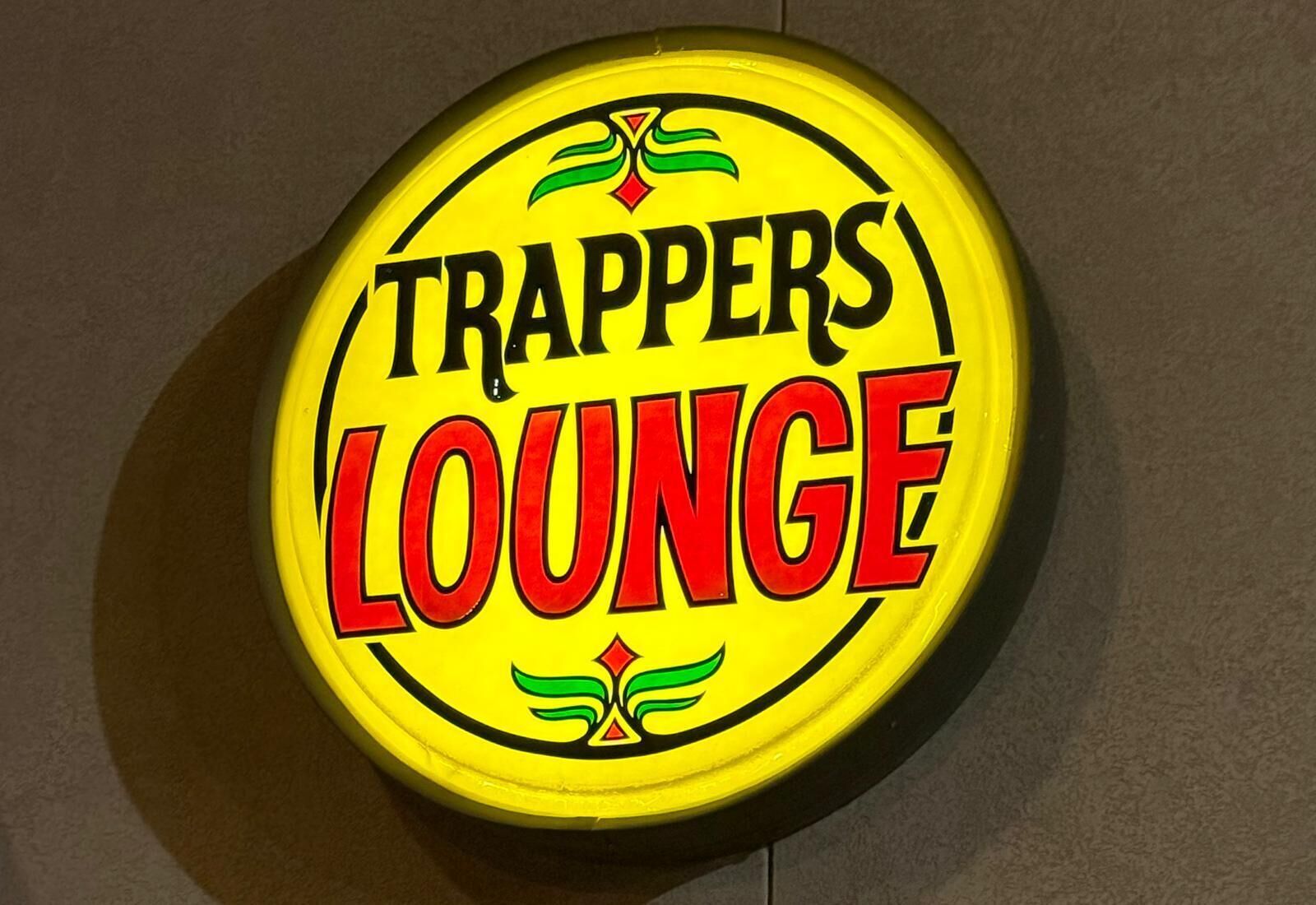 Un letrero circular con la inscripción 'TRAPPERS LOUNGE' en letras negritas.