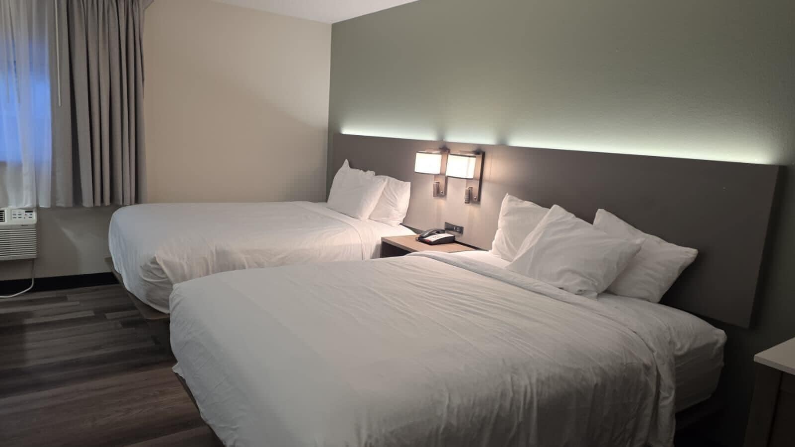 Una camera d'albergo con due letti, un comodino con una lampada e un condizionatore d'aria a parete.