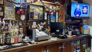 Un bar avec un comptoir en bois, différentes bouteilles d’alcool, un téléviseur et une enseigne sur laquelle on peut lire « TRAPPERS ».