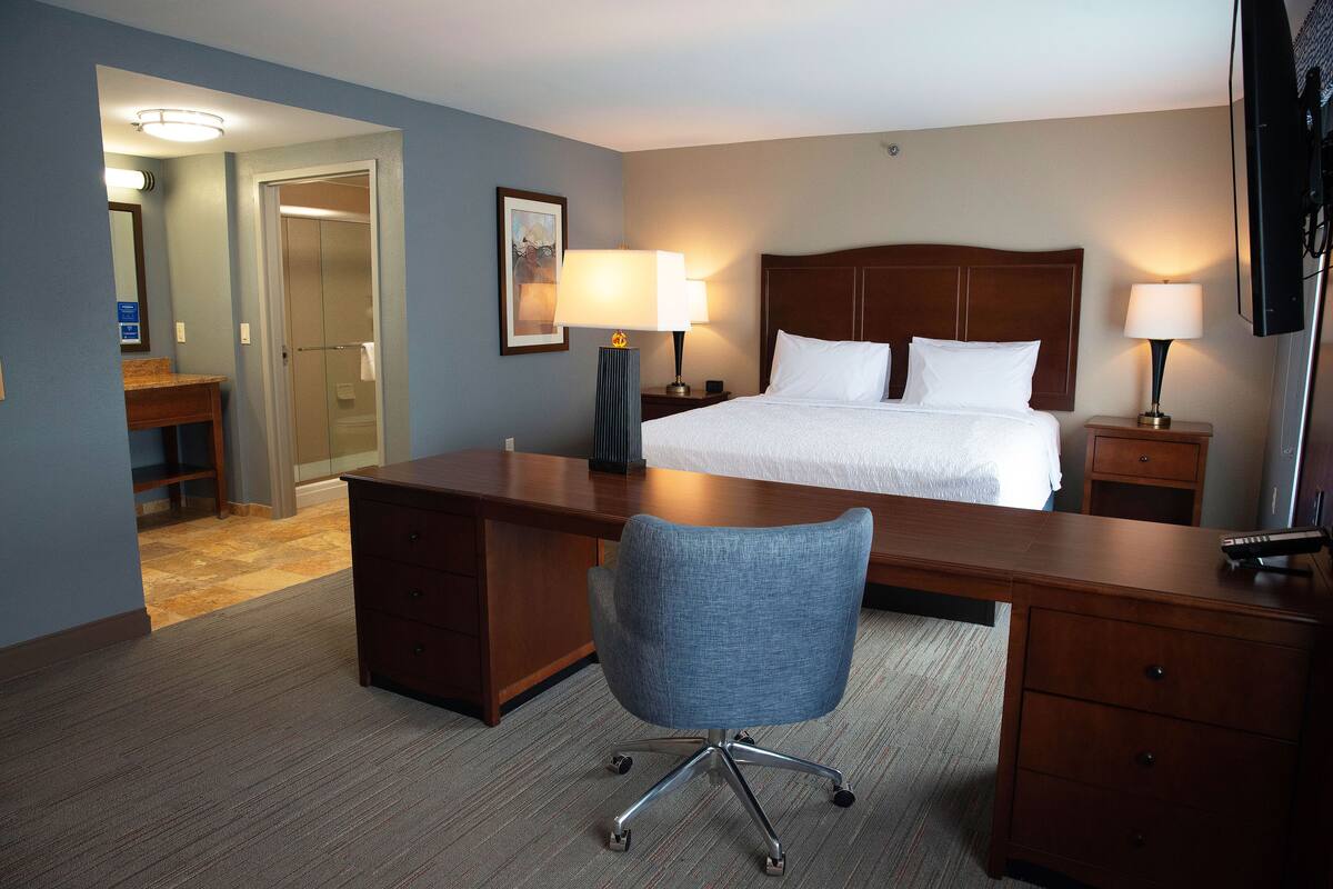 A hotel room with a bed, desk, chair, and two bedside lamps.
