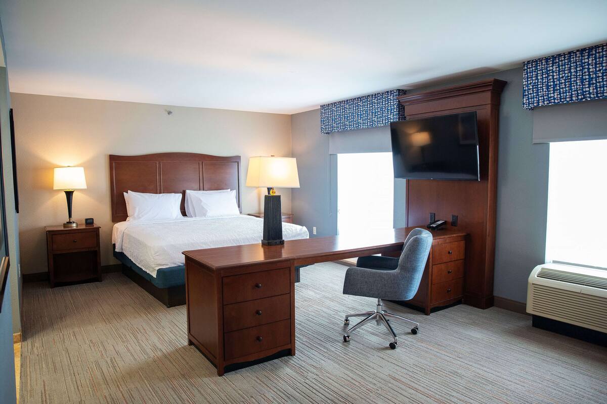 A hotel room with a bed, a desk, a chair, a TV, and a window.