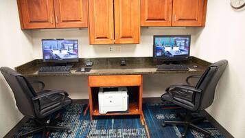 A conference room with two monitors, two black office chairs, a printer, and wooden cabinets.