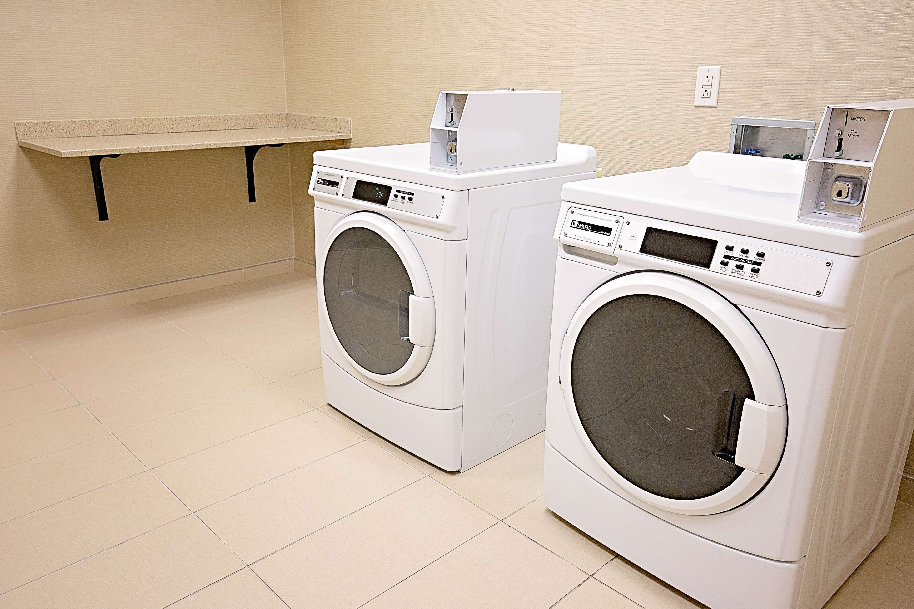 Two front-loading washing machines in a laundry room with a bench and a wall socket.