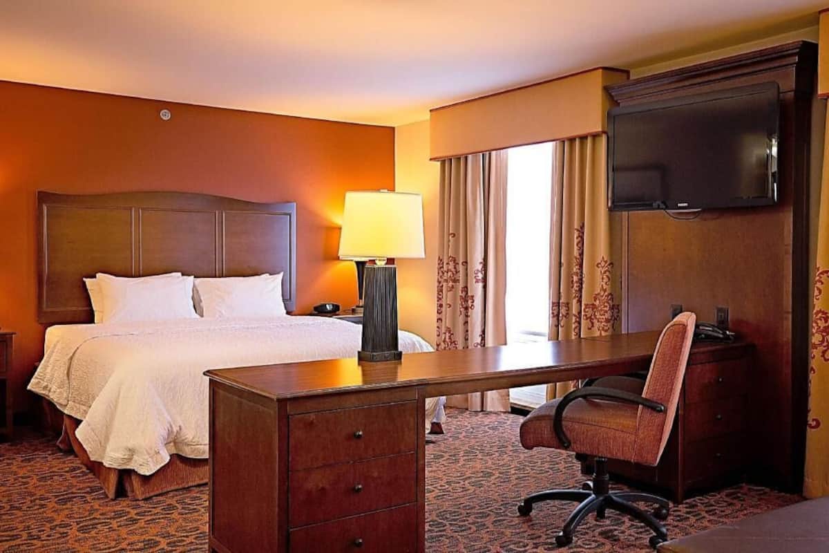A hotel room with a bed, desk, chair, lamp, TV, and curtains.