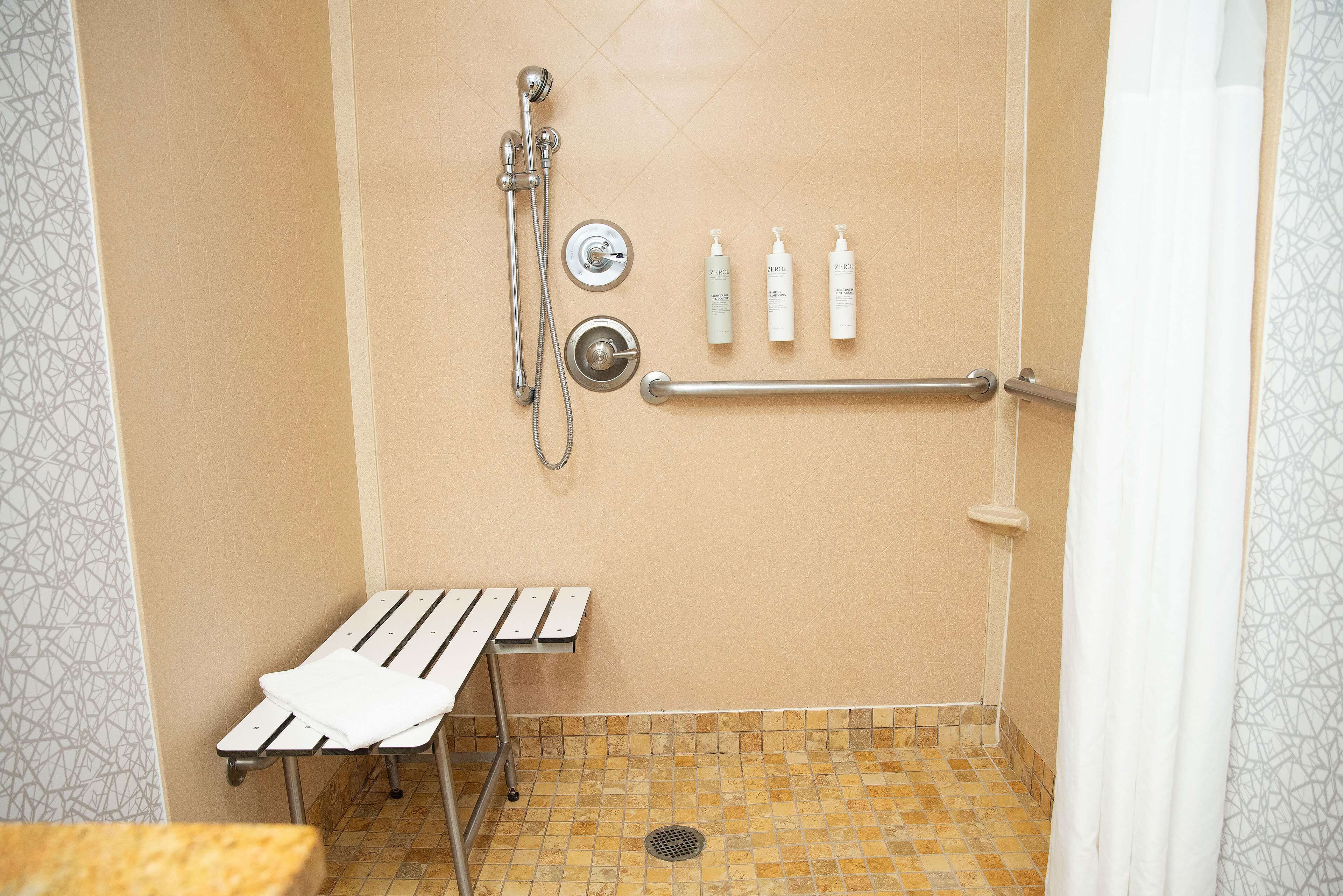 Uma área de chuveiro com barra de apoio, um banco e três frascos de shampoo.