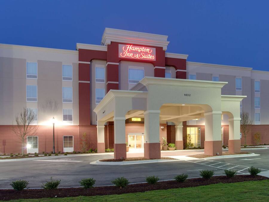 A Hampton Inn & Suites hotel with a prominent entrance, a parking lot, and a well-maintained lawn area.