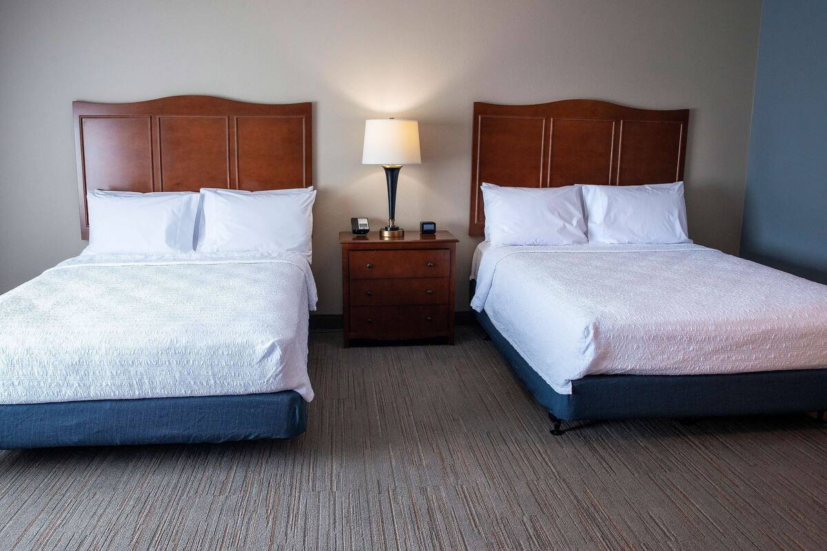 A hotel room with two beds, a nightstand with a lamp, and a carpeted floor.