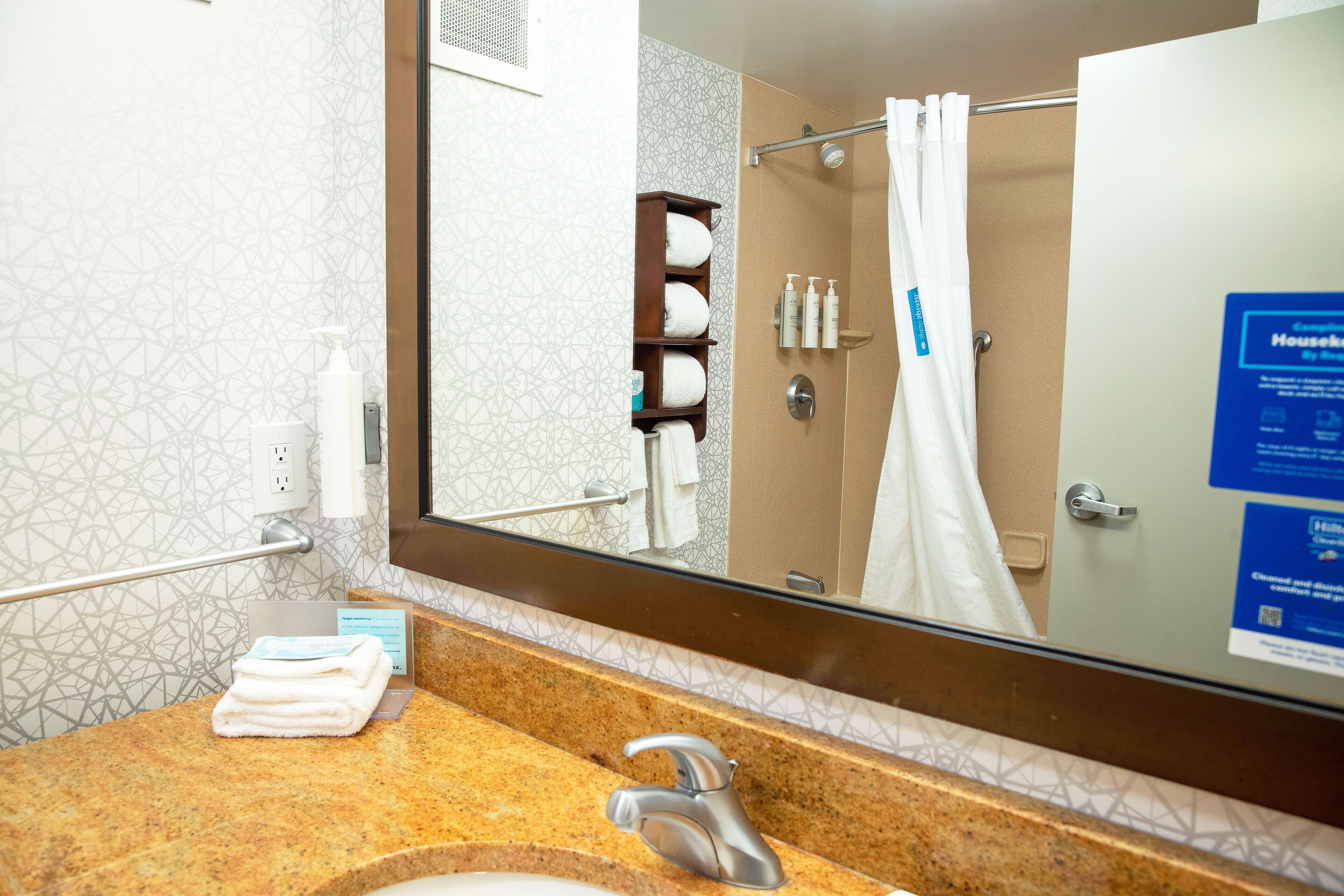 A bathroom with a granite countertop, a sink, a mirror, and a shower area.