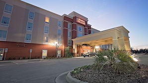 A hotel entrance with a covered driveway, a parking area, and a sign for Hampton Inn & Suites.