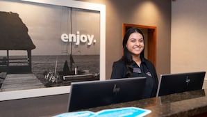 A reception desk with two HP computers, a large poster with the word "enjoy." and a beach scene, and a wooden door in the background.
