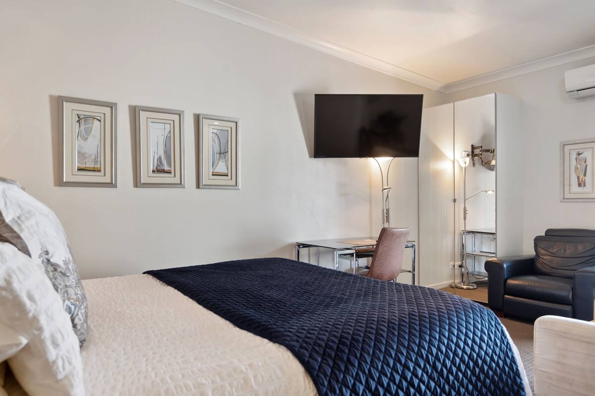 Una habitación de hotel con cama, escritorio, silla, televisor y cuadros en la pared.