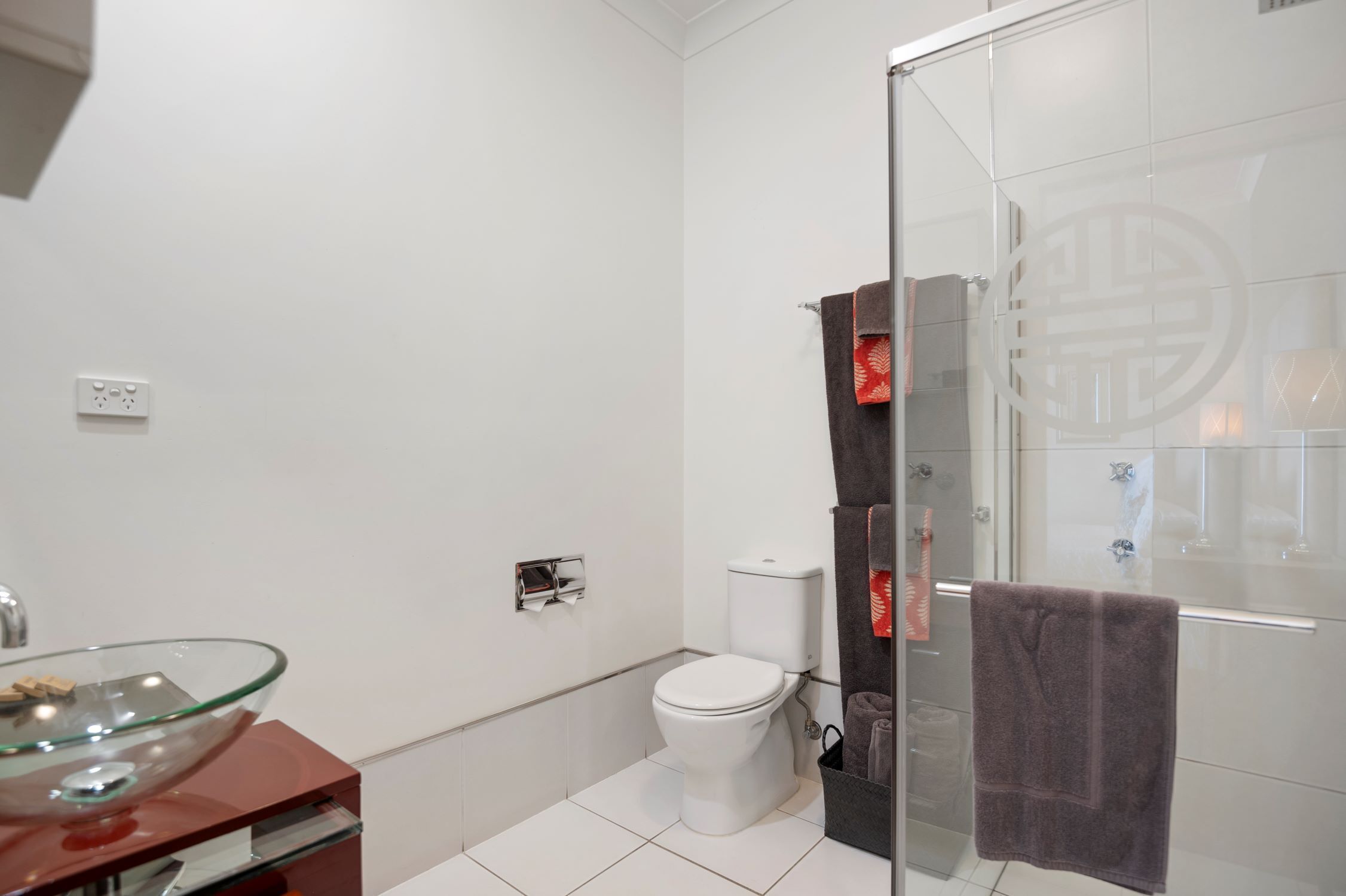 A modern bathroom with a glass shower enclosure, a glass sink, and a toilet.