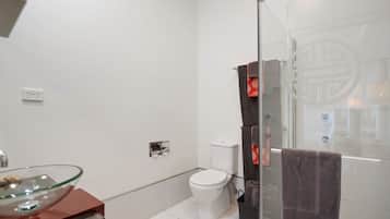 A modern bathroom with a glass shower enclosure, a glass sink, and a toilet.