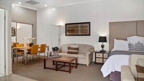 A modern hotel room with a bed, a sofa, a dining table with chairs, a small table with a tray, a lamp, and a framed picture on the wall. - 53 on Victoria (Warwick)
