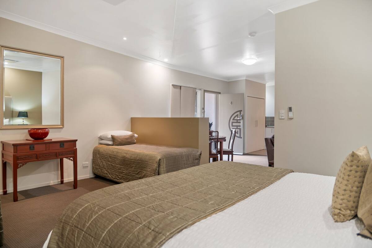 Una habitación de hotel con una cama grande, una mesita de noche con un tazón rojo, un espejo y una puerta que da a un baño.