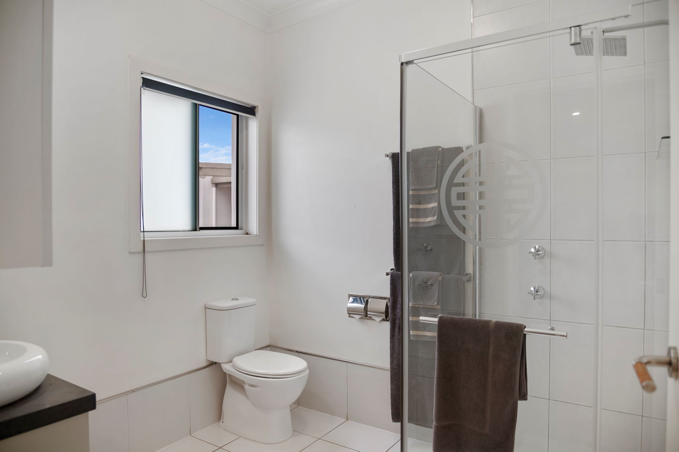 A modern bathroom with a toilet, a glass shower enclosure, and a window providing natural light.