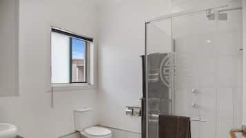 Un baño moderno con inodoro, cabina de ducha de vidrio y ventana que proporciona luz natural.
