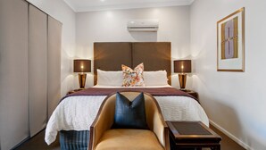 A hotel room with a large bed, two bedside lamps, a chair, a small table, and an air conditioning unit. - 53 on Victoria (Warwick)