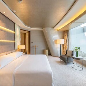 A modern hotel room with a large bed, a seating area with a small table and chairs, and a large window offering a view.