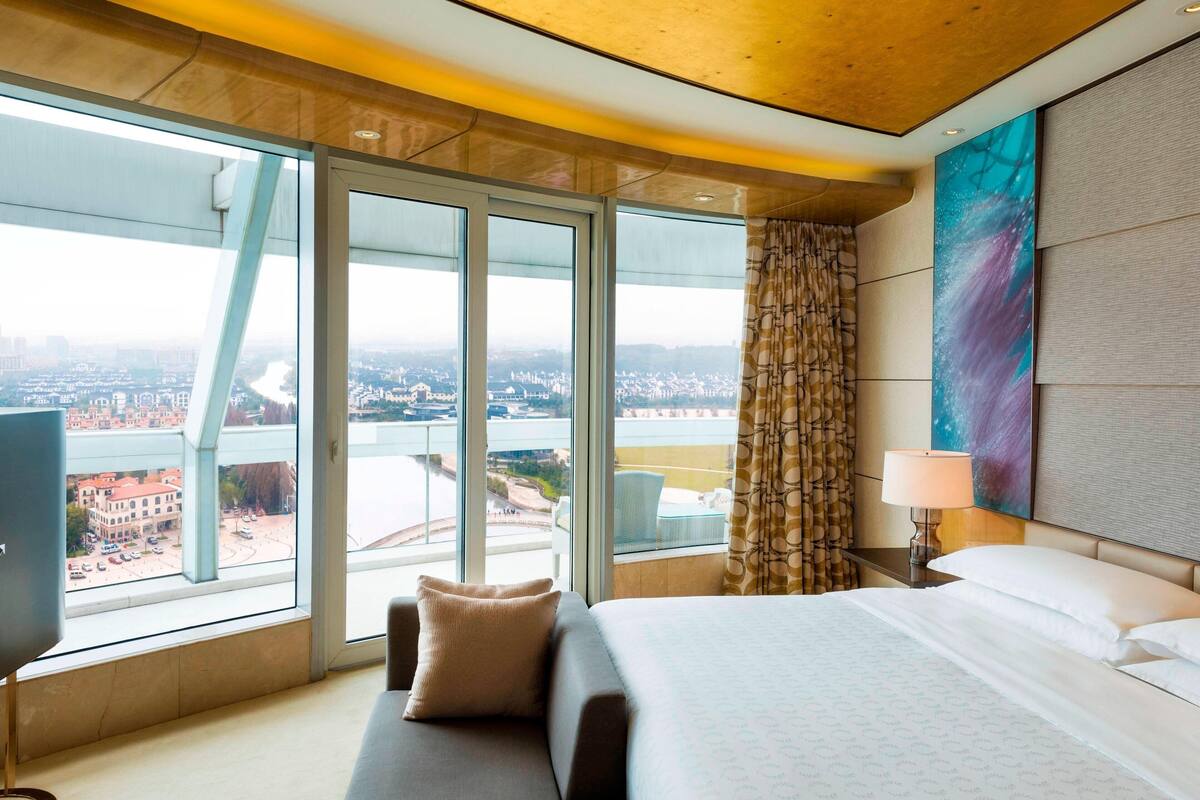 A hotel room with a large bed, a TV, a view of a cityscape, and a modern design.