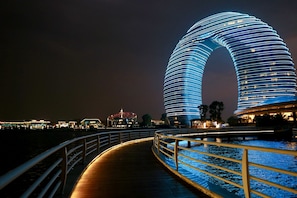 A waterfront promenade with a distinctive arched building and a wooden walkway.