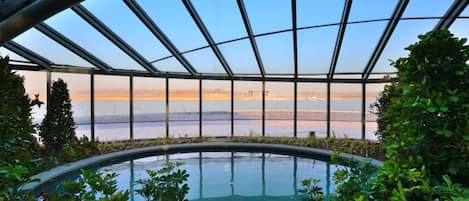 Une piscine à débordement, entourée de parois en verre, offrant une vue sur une étendue d’eau et un paysage lointain.
