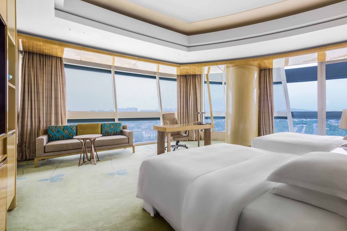 A hotel room with a large bed, a sofa, a desk, and a view of the city.
