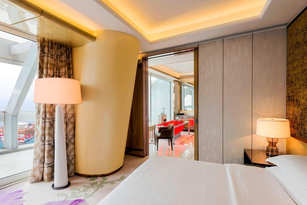 A hotel room with a bed, a desk, and a red bathtub.