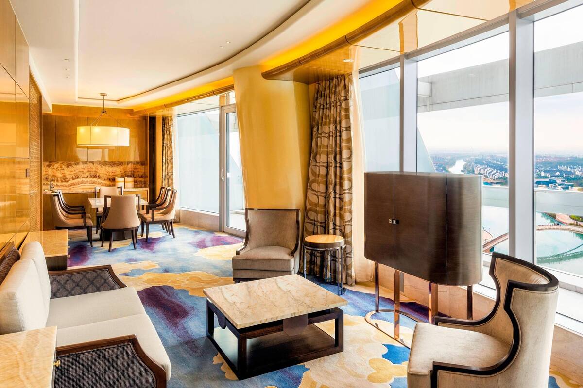 A modern hotel lobby with a seating area, a television, and large windows offering a city view.