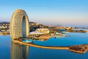 A modern hotel with a distinctive curved architecture, situated by a body of water with a pool and a marina. - Sheraton Huzhou Taihu Lake Hot Spring Resort & Spa (Huzhou)