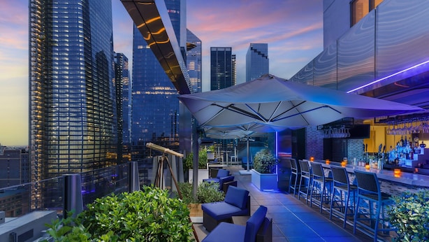 Een dakterras met terras, een bar en uitzicht op stadsflats.
