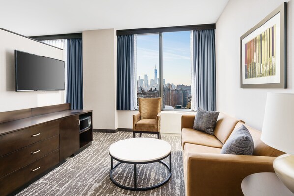 Une chambre d’hôtel moderne dotée d’une grande fenêtre donnant sur la ville, d’un téléviseur à écran plat, d’un canapé, d’un fauteuil et d’une table basse.