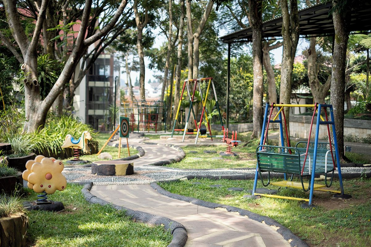 A playground with swings and a slide, surrounded by trees and a paved path.