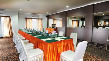 Un salón de conferencias con una larga mesa, sillas blancas y un mantel verde.