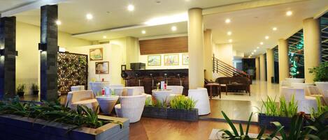 A spacious lobby with a wooden reception desk, comfortable seating areas, and a staircase leading to upper floors.