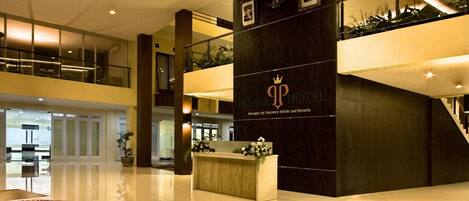 A modern hotel lobby with a reception desk, a large decorative rug, and a staircase leading to upper floors.